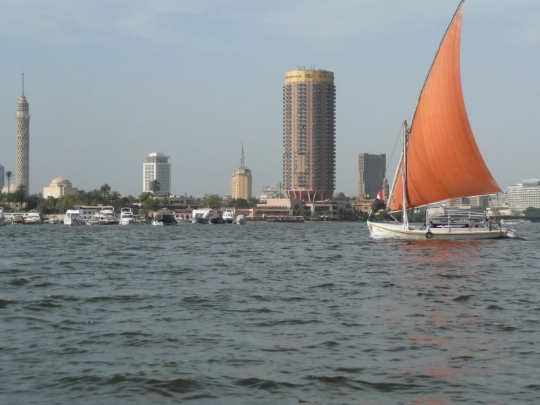 Segelboot mit orangefarbenem Segel auf dem Nil vor Kairos Ufer