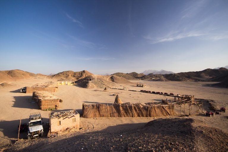 Desert visitor camp with shaded structures and a parked jeep