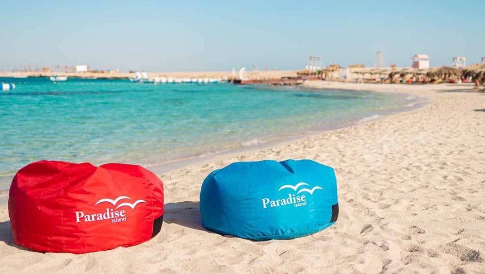 Red and blue Paradise Island beanbags beside the sandy beach and turquoise sea