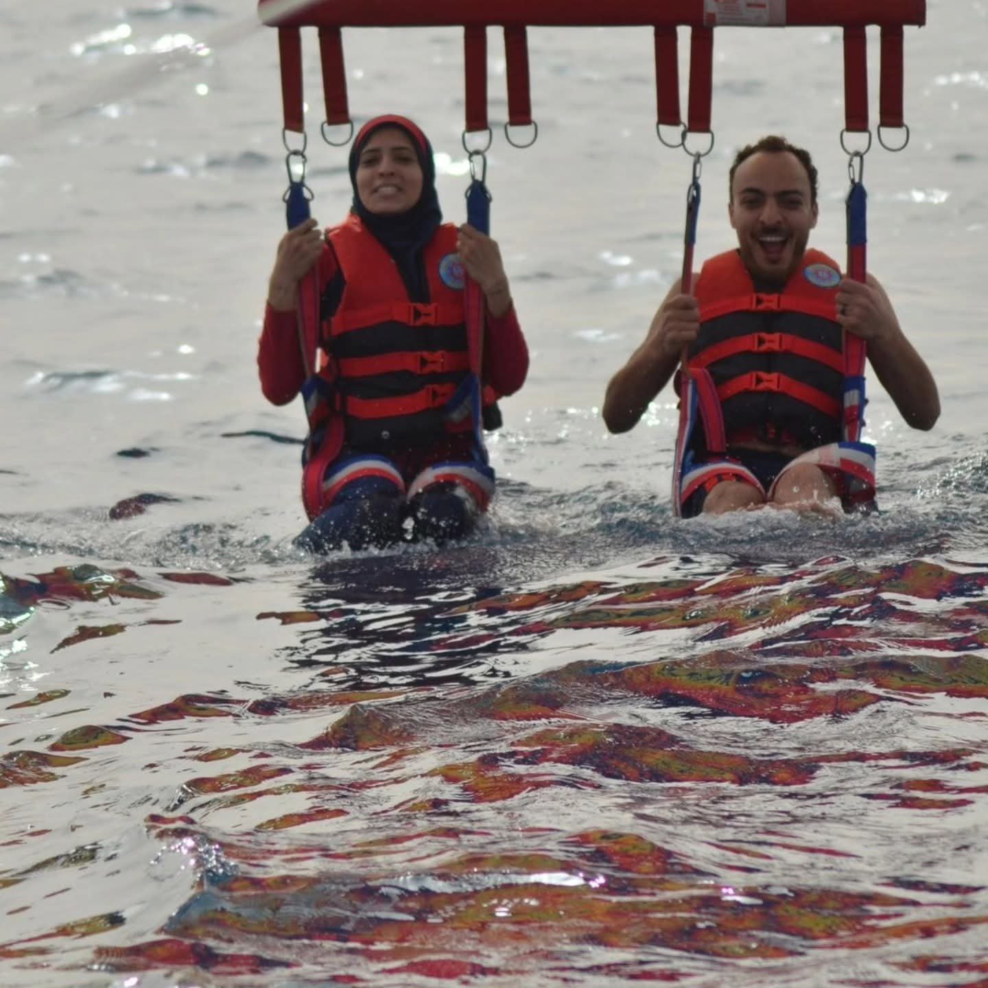 Zwei Gäste mit Schwimmwesten und Parasailing-Gurten über dem Wasser