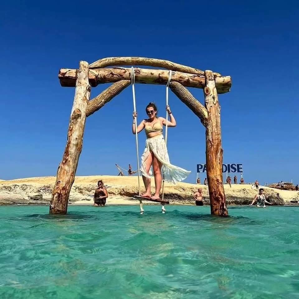 Besucherin auf einer Holzschaukel im flachen Wasser vor Paradise Island