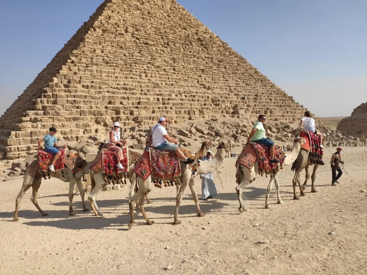 Besucher auf Kamelen vor einer Pyramide von Gizeh
