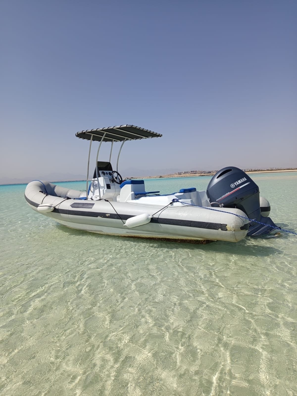 Small speedboat with a sun canopy anchored in shallow turquoise water