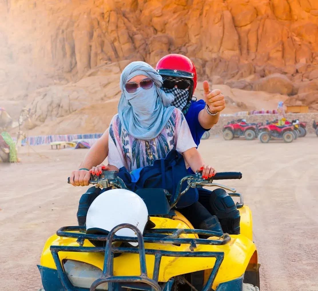 Two riders wearing helmets on a quad bike in the desert