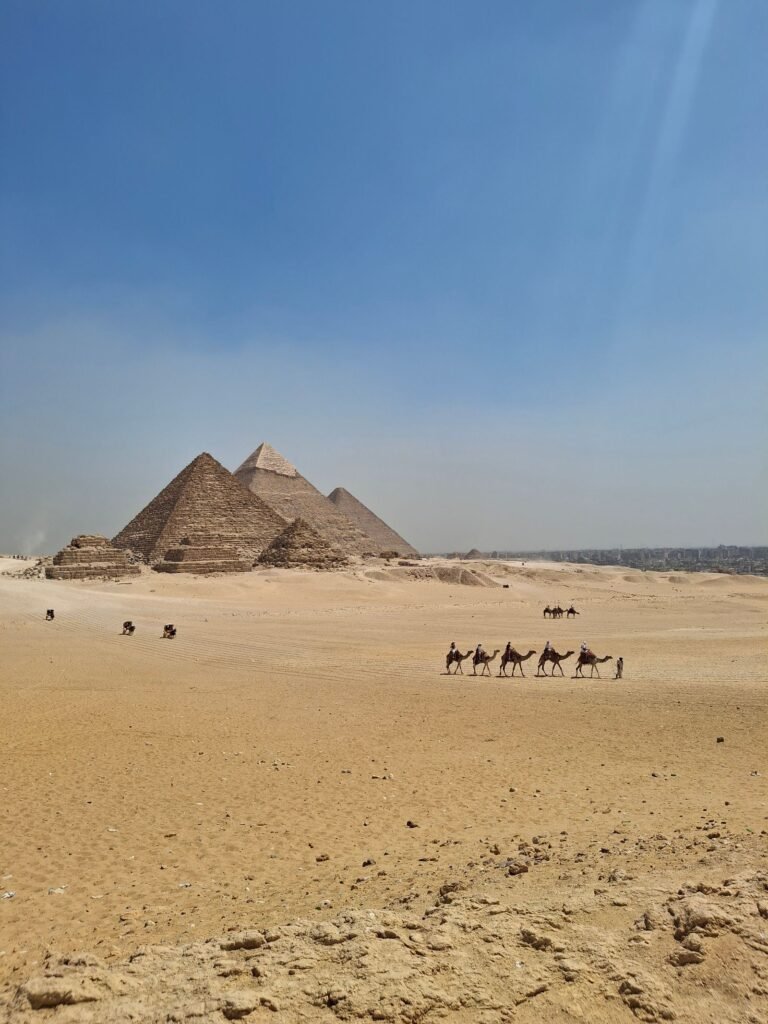 Blick über die Wüste auf die Pyramiden mit einer Karawane im Vordergrund
