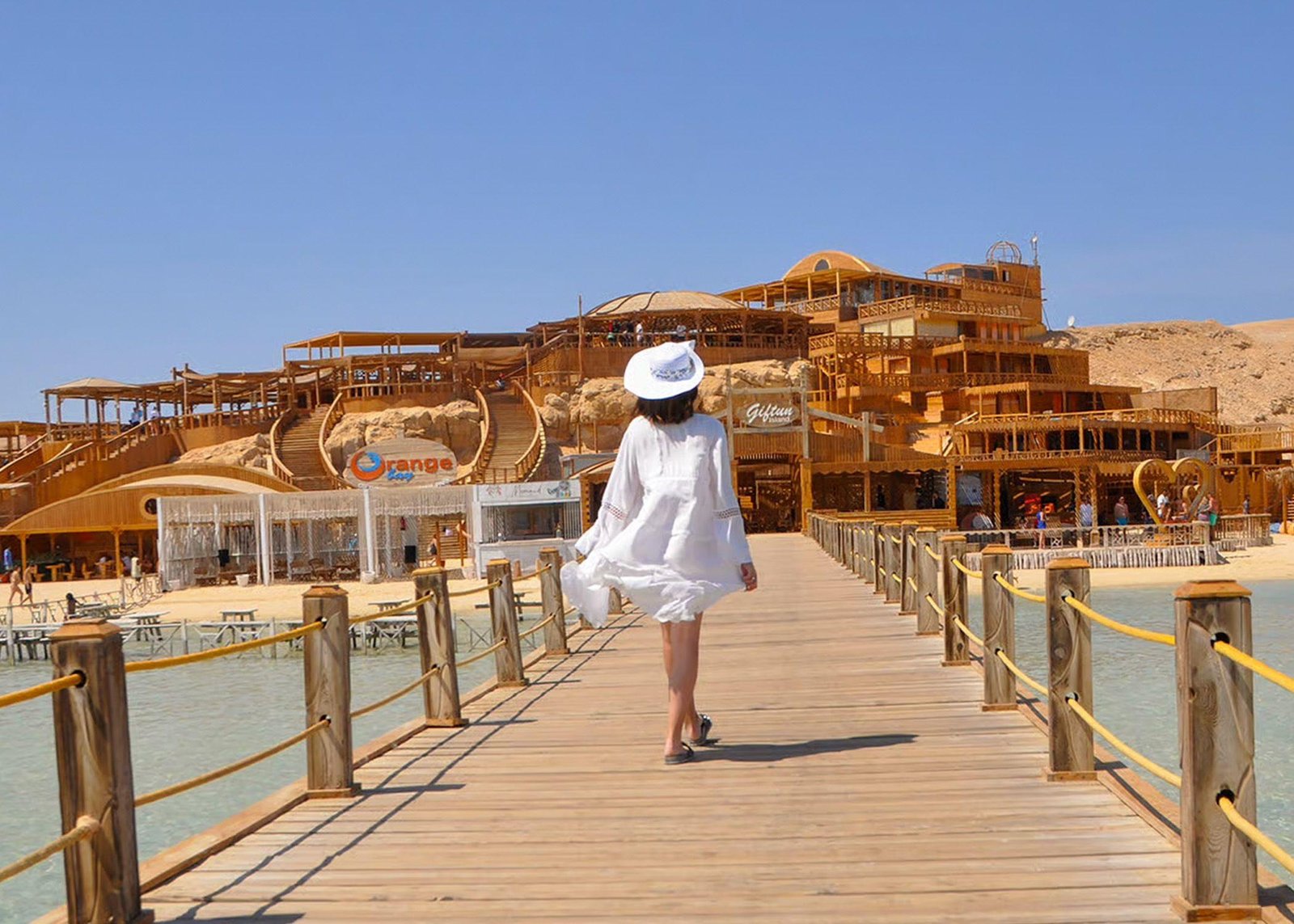 Besucherin auf dem Holzsteg vor den Gebäuden von Orange Bay Hurghada
