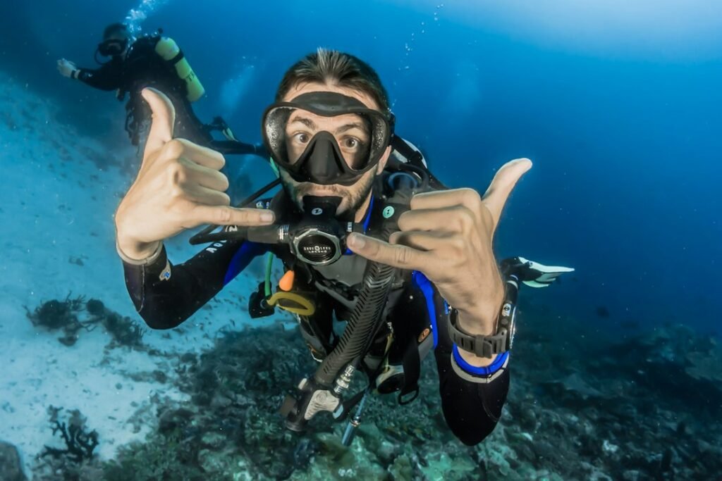 Taucher mit Maske und Atemregler zeigt Gesten vor der Unterwasserkamera
